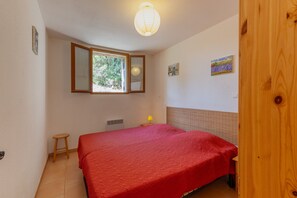 Een kamer met een bed, een raam, een spiegel, een klein krukje, een lamp en een deur.
