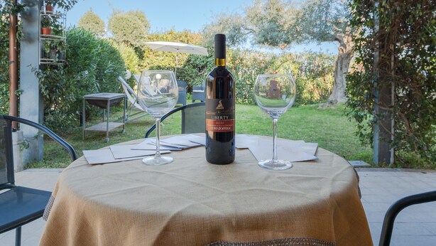 A table with a bottle of wine, two glasses, and a tablecloth in an outdoor setting with greenery in the background. - Holiday Home 'Ciumara East' with Private Terrace, Wi-Fi and Air Conditioning (Avola)