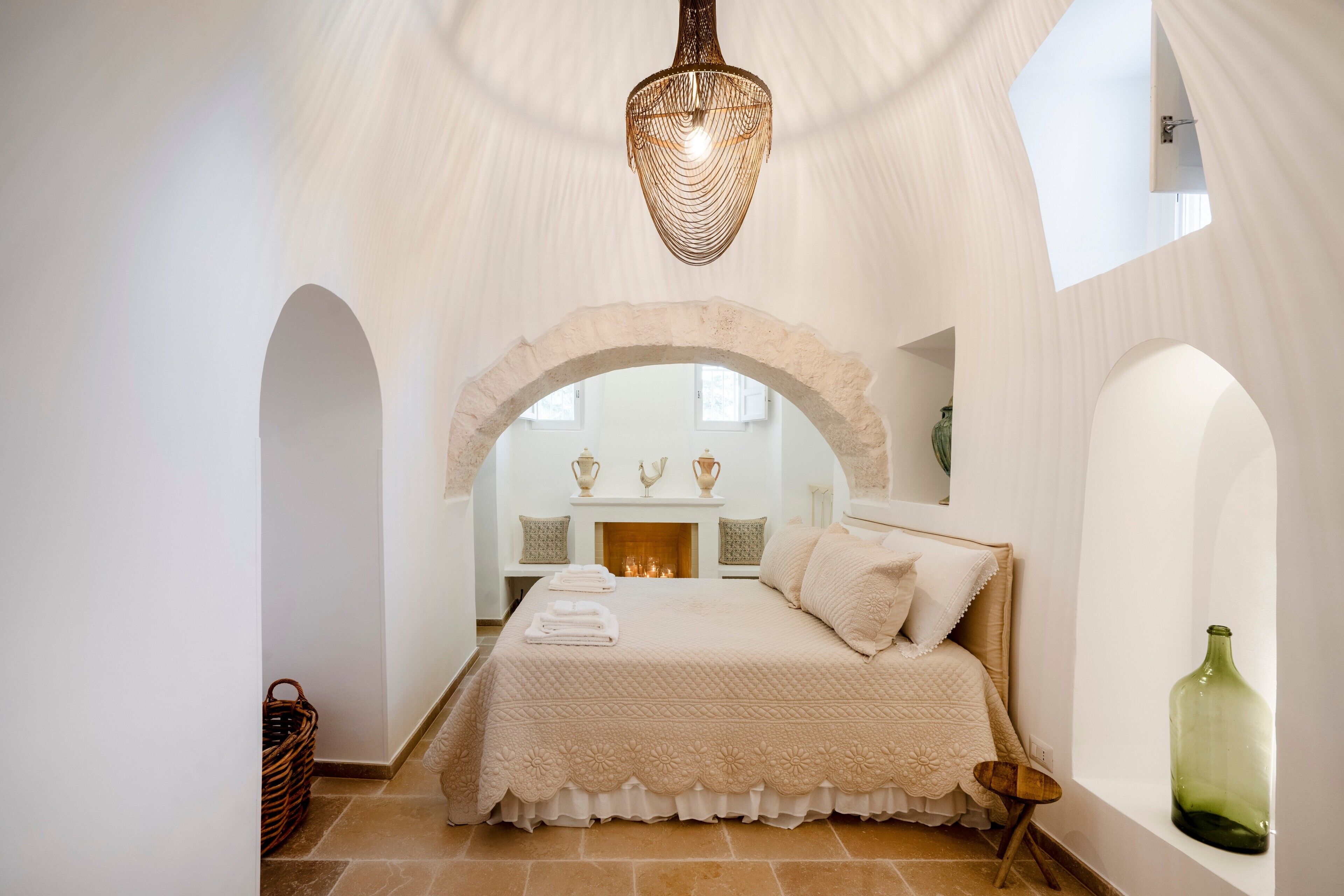 Une chambre à coucher avec un lit, un luminaire suspendu, une cheminée et une porte en arc de cercle.