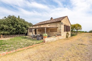 A stone house with a tiled roof, a covered patio with outdoor furniture, and a well-maintained lawn.