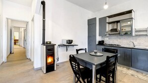 Una cocina moderna con estufa de leña, armarios grises y un comedor con sillas.