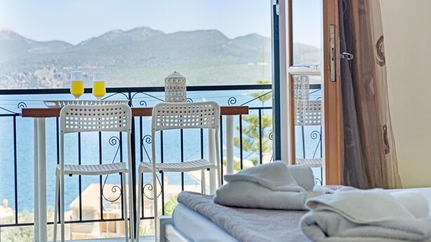 A balcony with two white chairs, a table, and two glasses of orange juice.