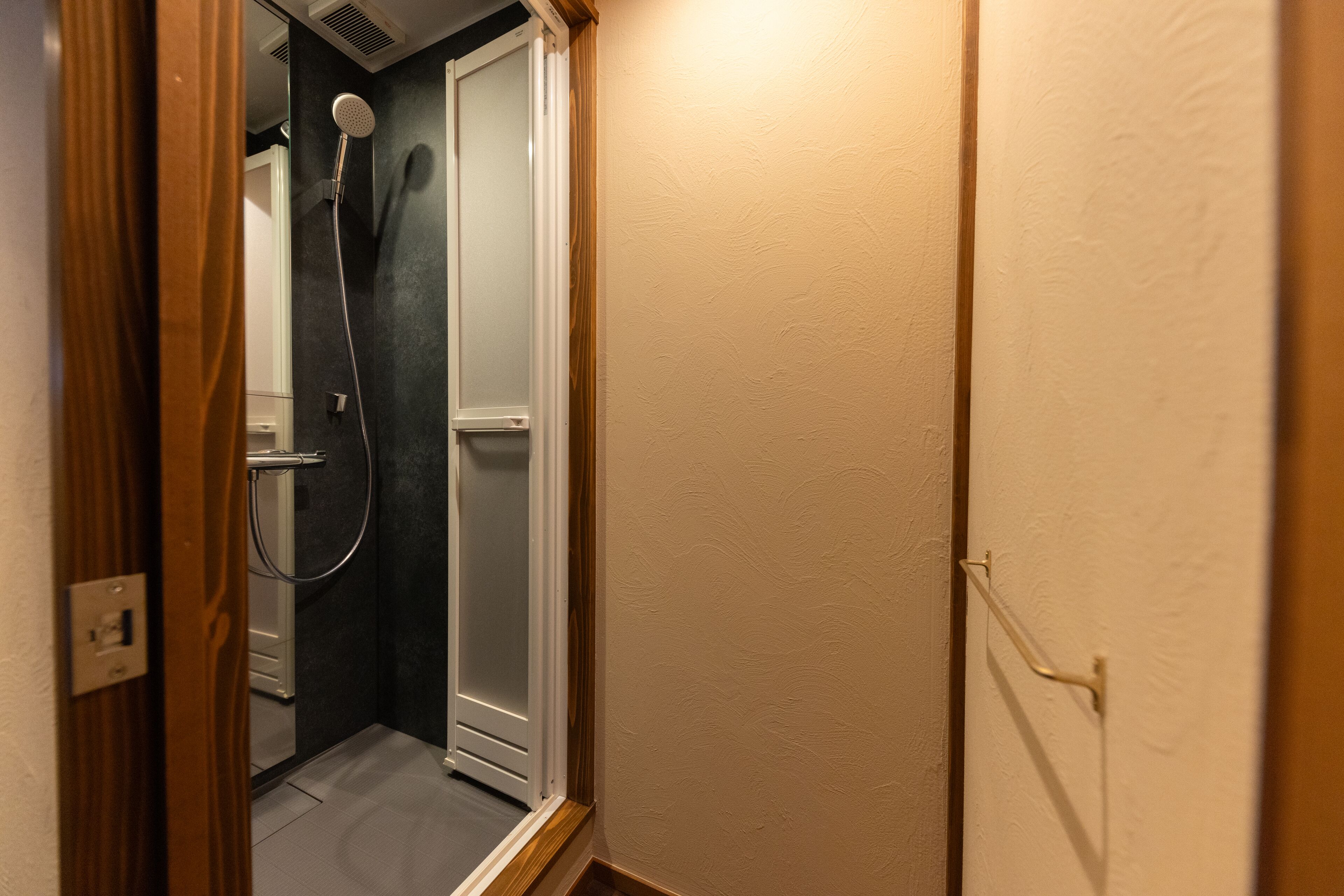 A narrow hallway with a shower area on the left, a wooden door frame, and a light switch on the wall.