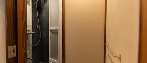 Un pasillo estrecho con una zona de ducha a la izquierda, un marco de puerta de madera y un interruptor de luz en la pared.