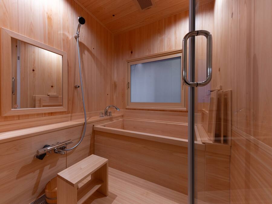 Een houten sauna met een glazen douchecabine, een bankje en een raam.