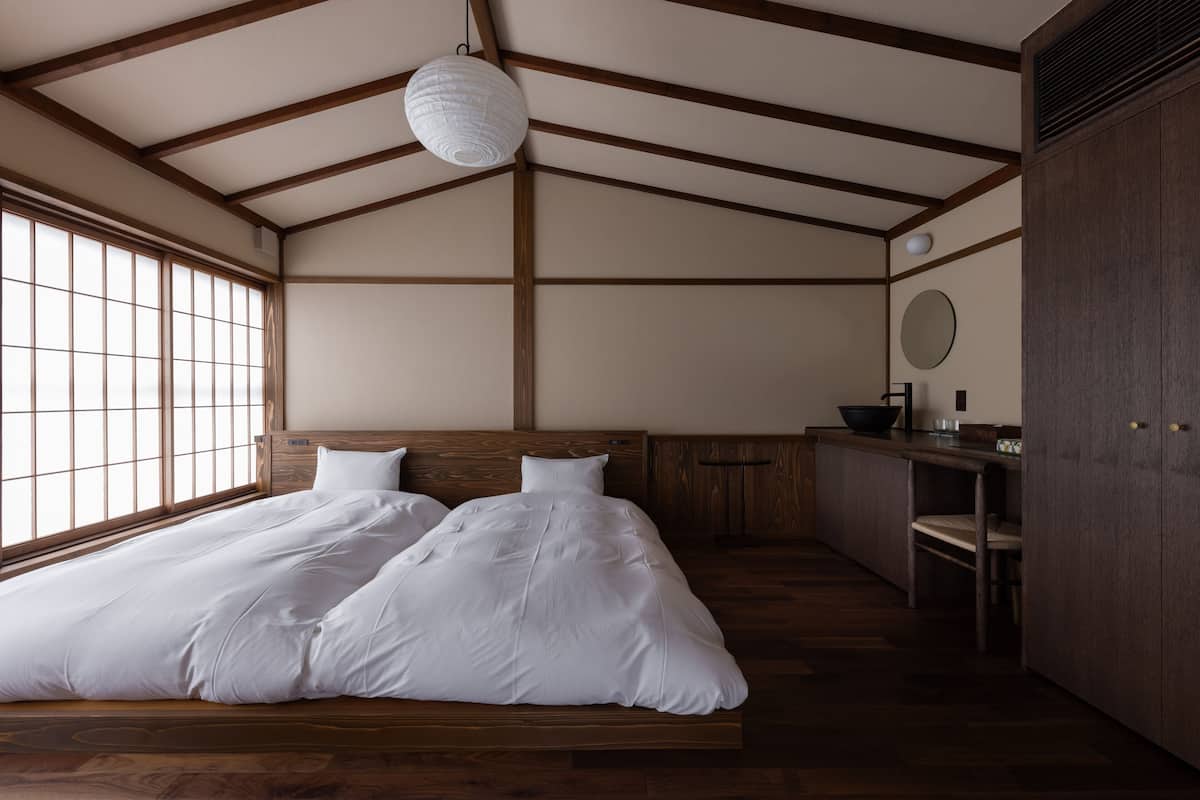 Una habitación con una cama grande, vigas de madera, un ventanal, una mesita y un armario.