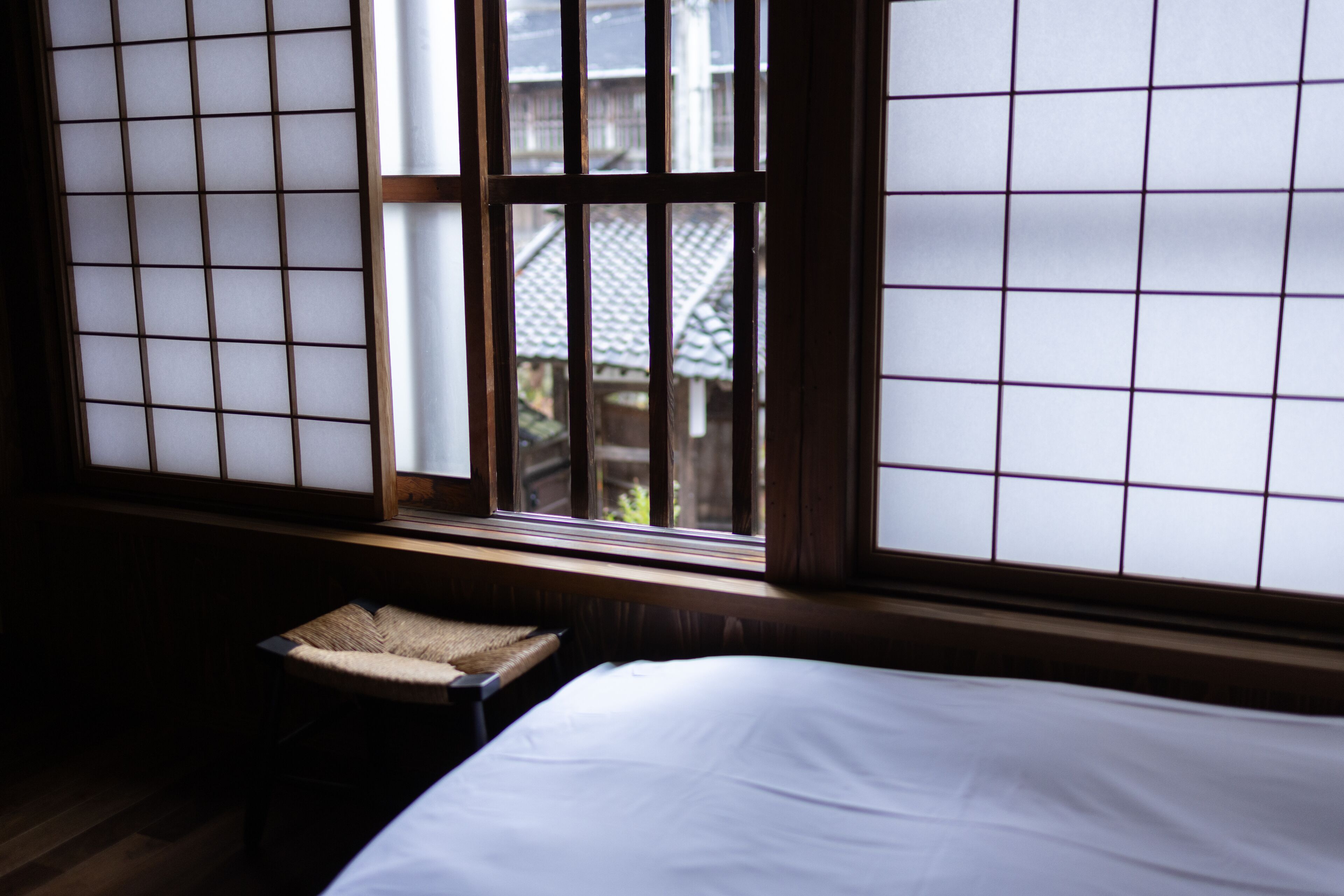 A traditional Japanese room with tatami flooring, a low wooden bench, and a bed with white bedding.