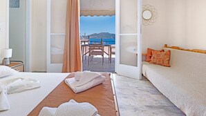 Une chambre d’hôtel avec un lit, un canapé, une vue sur la mer et un balcon aménagé avec du mobilier d’extérieur.