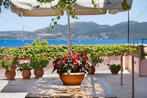 A terrace with a table, potted plants, and a view of the sea and mountains.