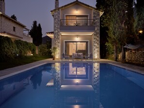 A two-story house with a swimming pool, stone facade, and outdoor seating area.