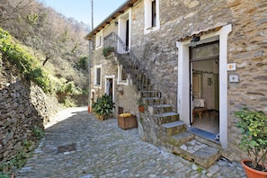 Un bâtiment en pierre avec un escalier menant à une porte, entouré de plantes en pot et bordé d’un chemin pavé.