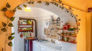 Une cuisine équipée d’une cuisinière à gaz, d’étagères en bois et d’un mur en pierre.