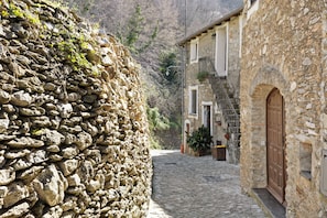 Une ruelle étroite pavée, bordée de bâtiments en pierre dotés de portes en arc de cercle et de balcons.