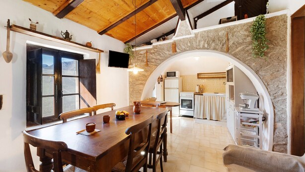 Un coin repas avec une table et des chaises en bois, un mur en pierre et une arche donnant sur la cuisine.