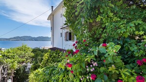 Ein weißes Gebäude mit Garten und Meerblick, mit Bergen im Hintergrund.