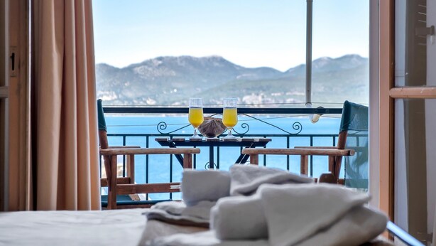 Un balcon avec une table et des chaises, deux verres de jus d’orange et une vue sur les montagnes et l’eau.