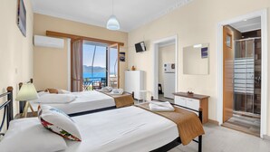 Une chambre d’hôtel avec deux lits, un bureau, une télévision et un balcon donnant sur la mer.