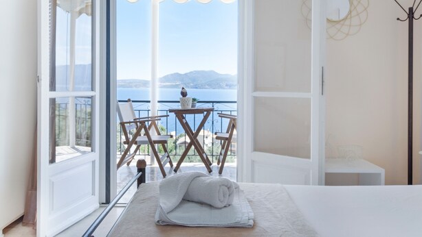 A room with a bed, a window with a view of the sea, and a balcony with chairs. - Studio Apartment 'Standard with Sea View 6' with Sea View, Wi-Fi and Air Conditioning (Nikiana)