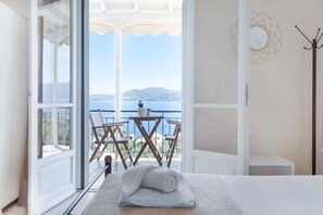 A room with a bed, a window with a view of the sea, and a balcony with chairs. - Studio Apartment 'Standard with Sea View 6' with Sea View, Wi-Fi and Air Conditioning (Nikiana)