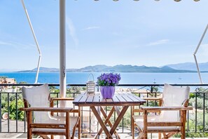Un balcon avec deux chaises en bois, une petite table, une plante en pot et une vue sur la mer et les montagnes.
