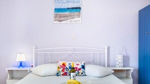 A bedroom with a bed, a nightstand with a lamp, a decorative pillow, a tray with bananas and a bottle, and a wall with a beach-themed poster.