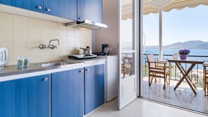 A modern kitchen with blue cabinets, a stainless steel sink, and a view of the sea through an open door.
