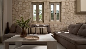 A living room with a stone wall, two windows, a sofa, a coffee table, and a vase with plants. - Villa 'Avesta Private Villas - Kallisto' with Sea View, Private Pool and Air Conditioning (Lefkada)