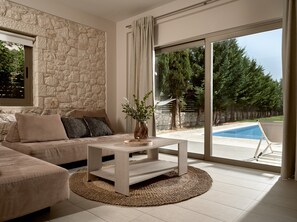 Ein modernes Wohnzimmer mit Steinwand, einem beigen Sofa, einem Couchtisch und Blick auf einen Swimmingpool.