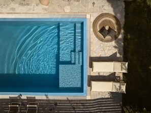 A rectangular swimming pool with clear blue water, surrounded by stone tiles and a grassy area with a woven basket.