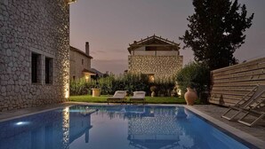 A swimming pool with lounge chairs, stone buildings, and a wooden fence. - Villa 'Iokasti' with Sea View, Private Pool, and Air Conditioning (Lefkada)
