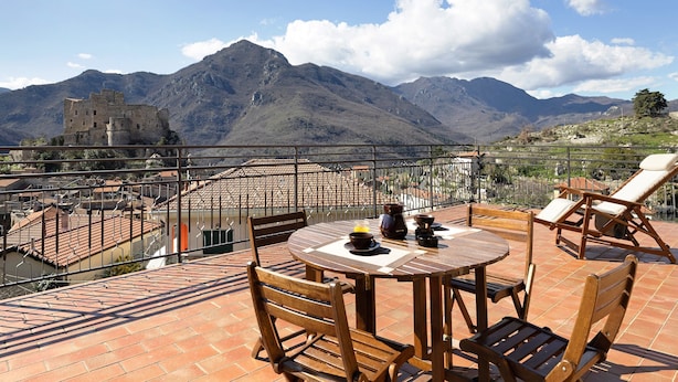 A terrace with a table and chairs, overlooking mountains and a castle. - Apartment 'La Terrazza Del Tempo' with Mountain View, Wi-Fi and Air Conditioning (Castelvecchio di Rocca Barbena)