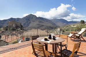 Una terraza con mesa y sillas, con vistas a montañas y un castillo.