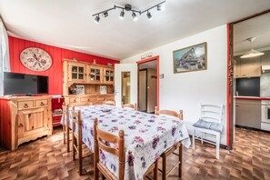 Ein Essbereich mit Tisch, Stühlen, einem Fernseher, Holzschränken und einer roten Wand.