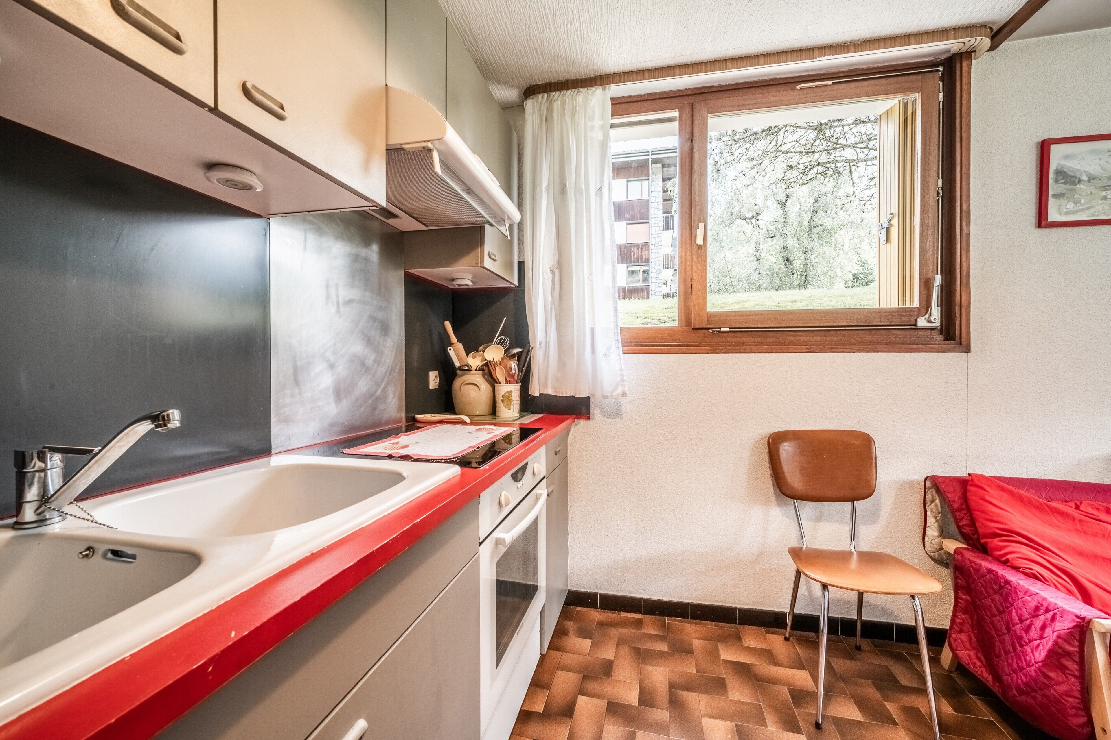 Een kleine keuken met een spoelbak, fornuis en raam.