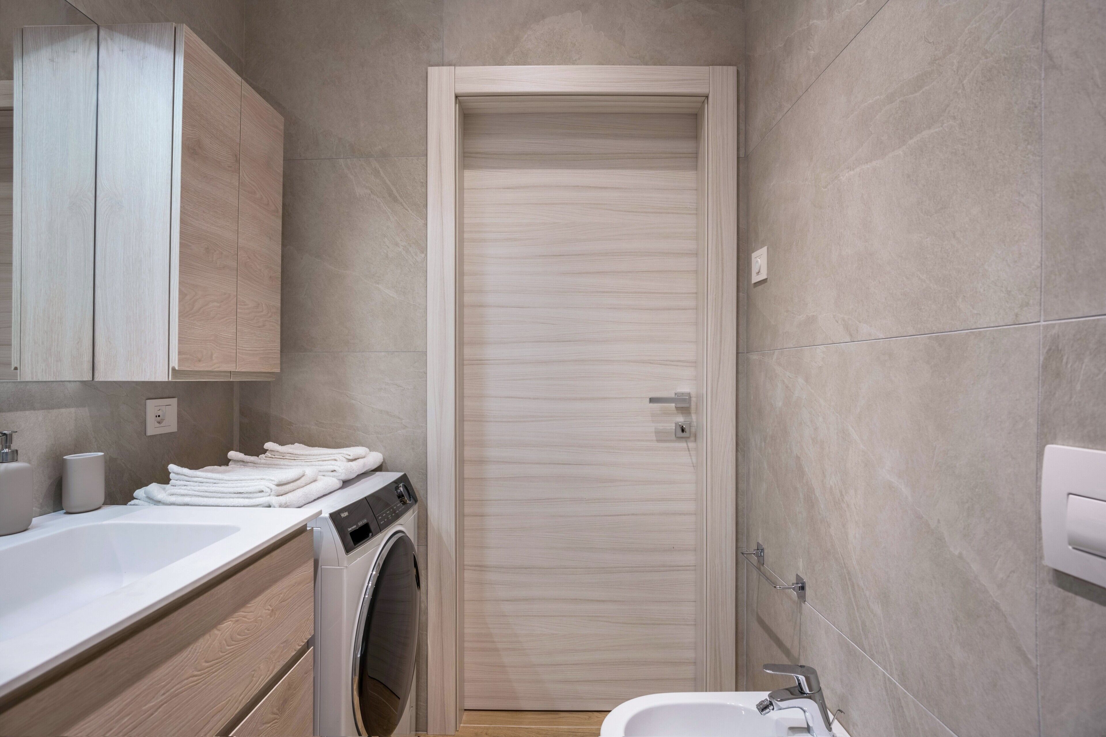 A compact bathroom with a washing machine, a sink, and a toilet.