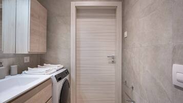 A compact bathroom with a washing machine, a sink, and a toilet.