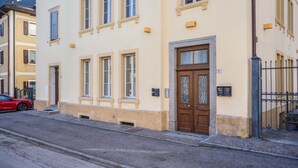 Vista de una calle con un edificio que destaca por su entrada, una puerta visible y una placa con un número.