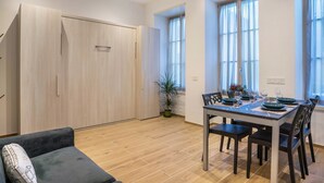Una zona de comedor con una mesa preparada para cuatro personas, un sofá, un armario de madera y una planta en maceta.