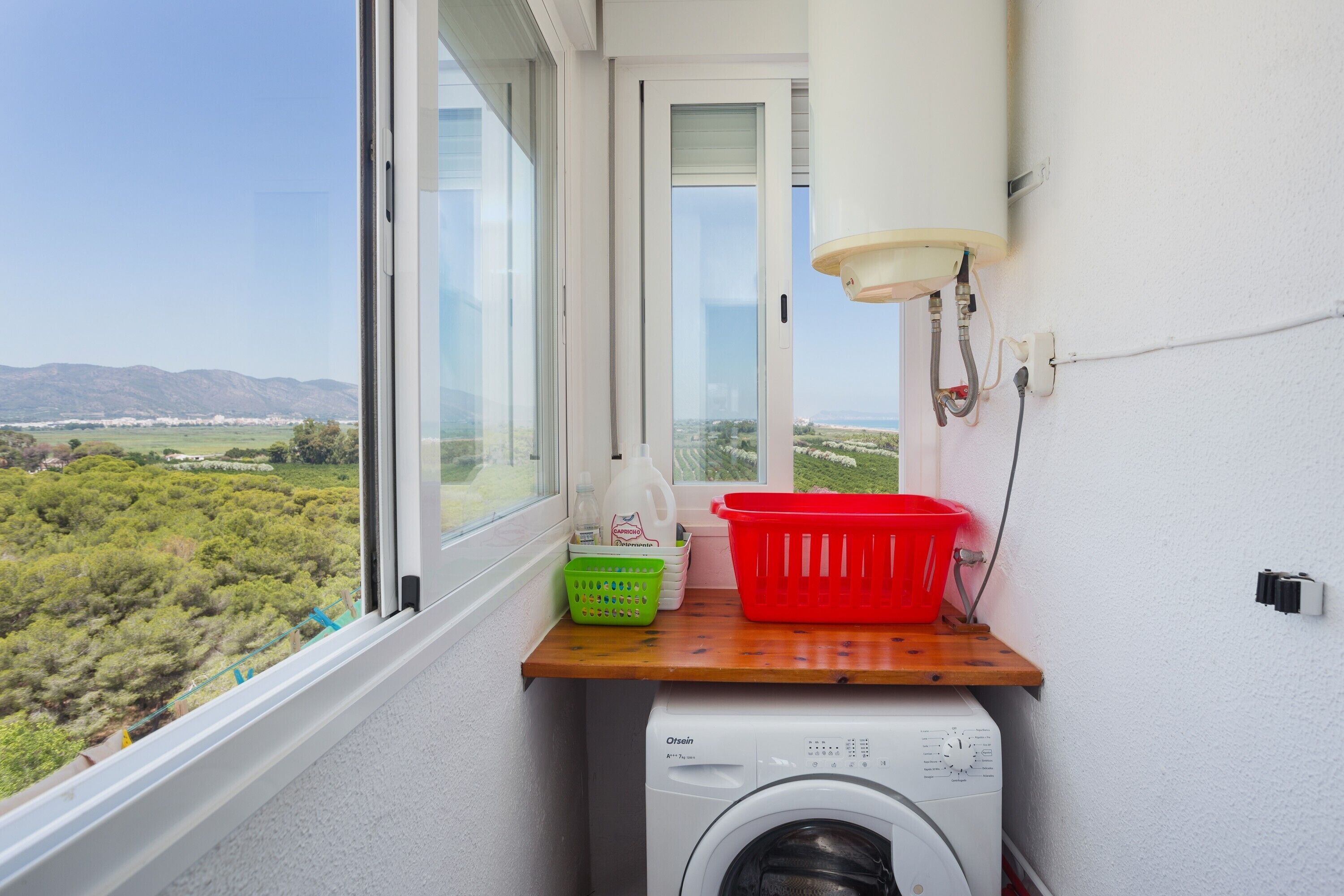 Ein Waschbereich mit Waschmaschine, einem Fenster mit Blick auf Grünflächen und Berge sowie einem Holzboden mit Wäschekörben.
