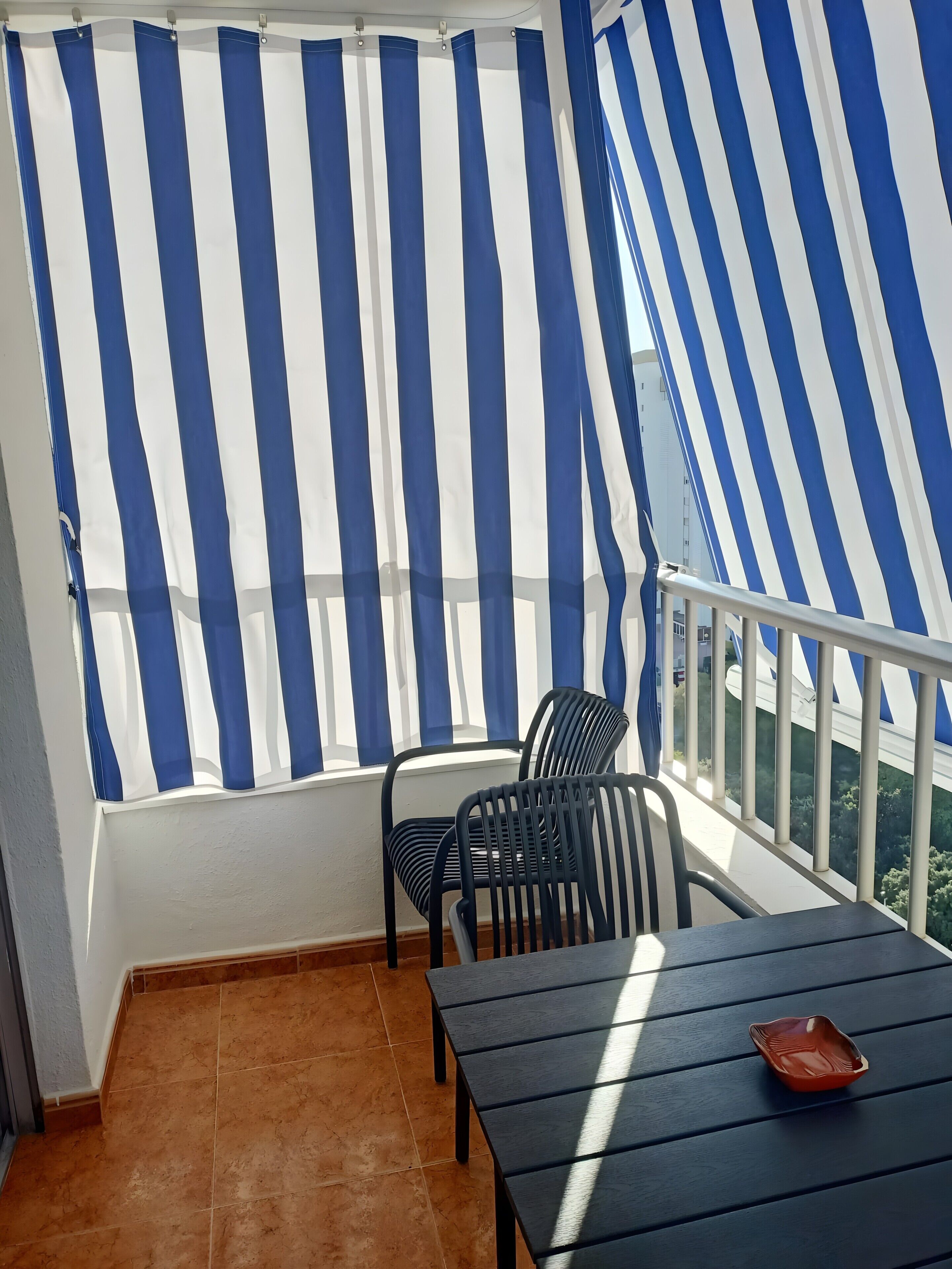 Uma varanda com cortinas listradas, uma mesa e duas cadeiras.