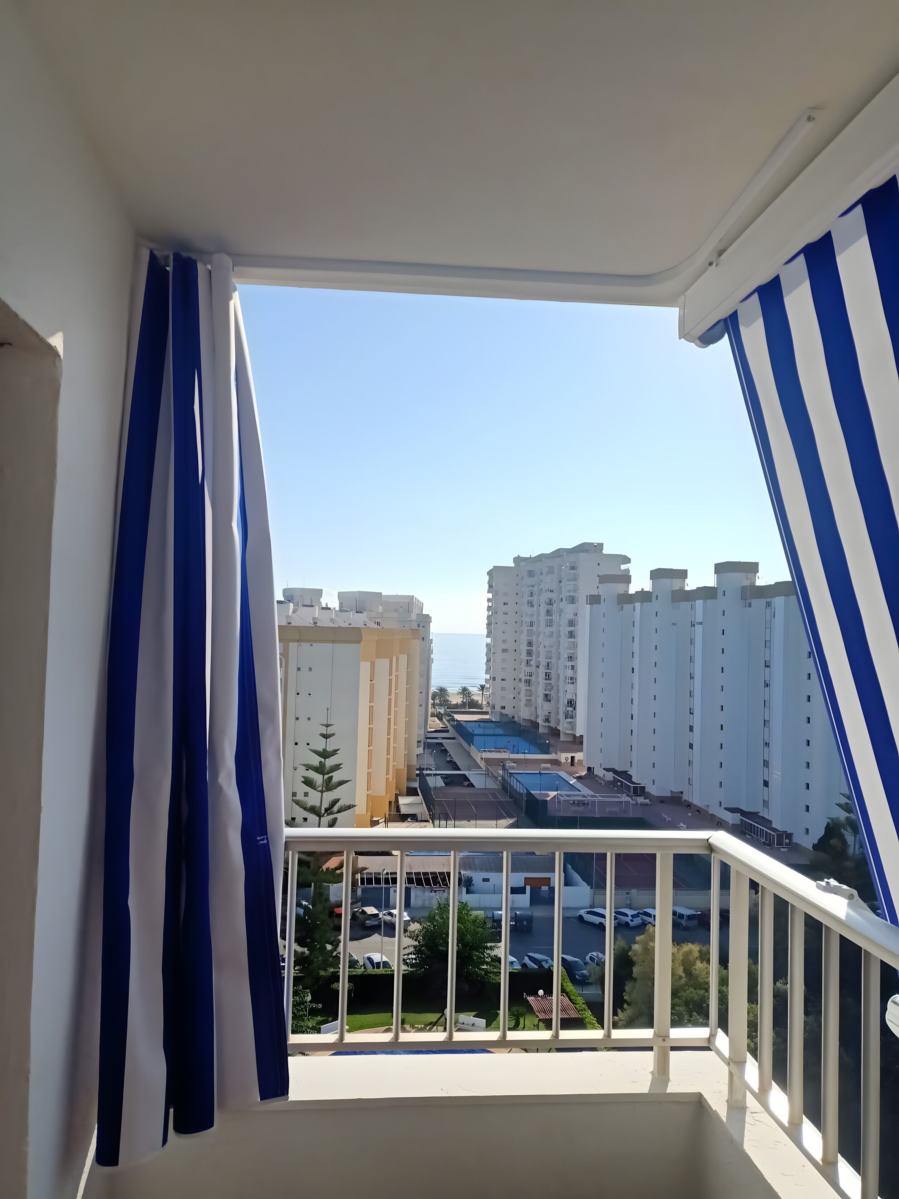 Un balcón con vista a edificios altos, una piscina y coches estacionados.