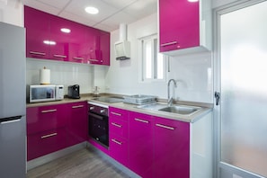 Een moderne keuken met roze kastjes, een magnetron, een koffiezetapparaat en een vaatwasser.