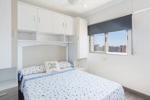 Een slaapkamer met een bed, een witte kledingkast en een raam met uitzicht op de stad.