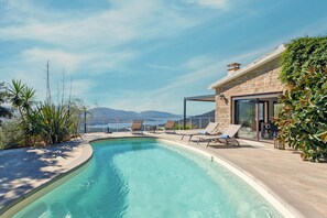 A swimming pool with lounge chairs, a stone building, and a view of the sea.