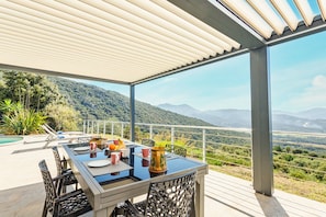 Área de refeições ao ar livre com uma mesa posta para dois, com vista para uma paisagem montanhosa.