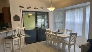 Un espace repas comprenant une table et des chaises, un luminaire au plafond et une porte donnant sur un balcon.