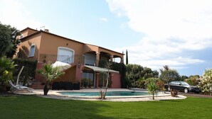 Une maison à deux étages avec une piscine, un patio couvert et une voiture garée dans l’allée.
