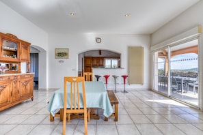 Un área de comedor con una mesa y sillas, un armario de madera y vistas a un patio exterior a través de una puerta de vidrio.