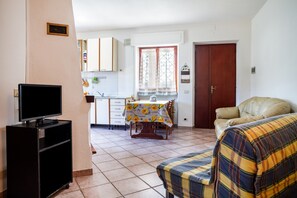 Una sala de estar con televisor, un sofá, una mesa de comedor con sillas y una cocina al fondo.