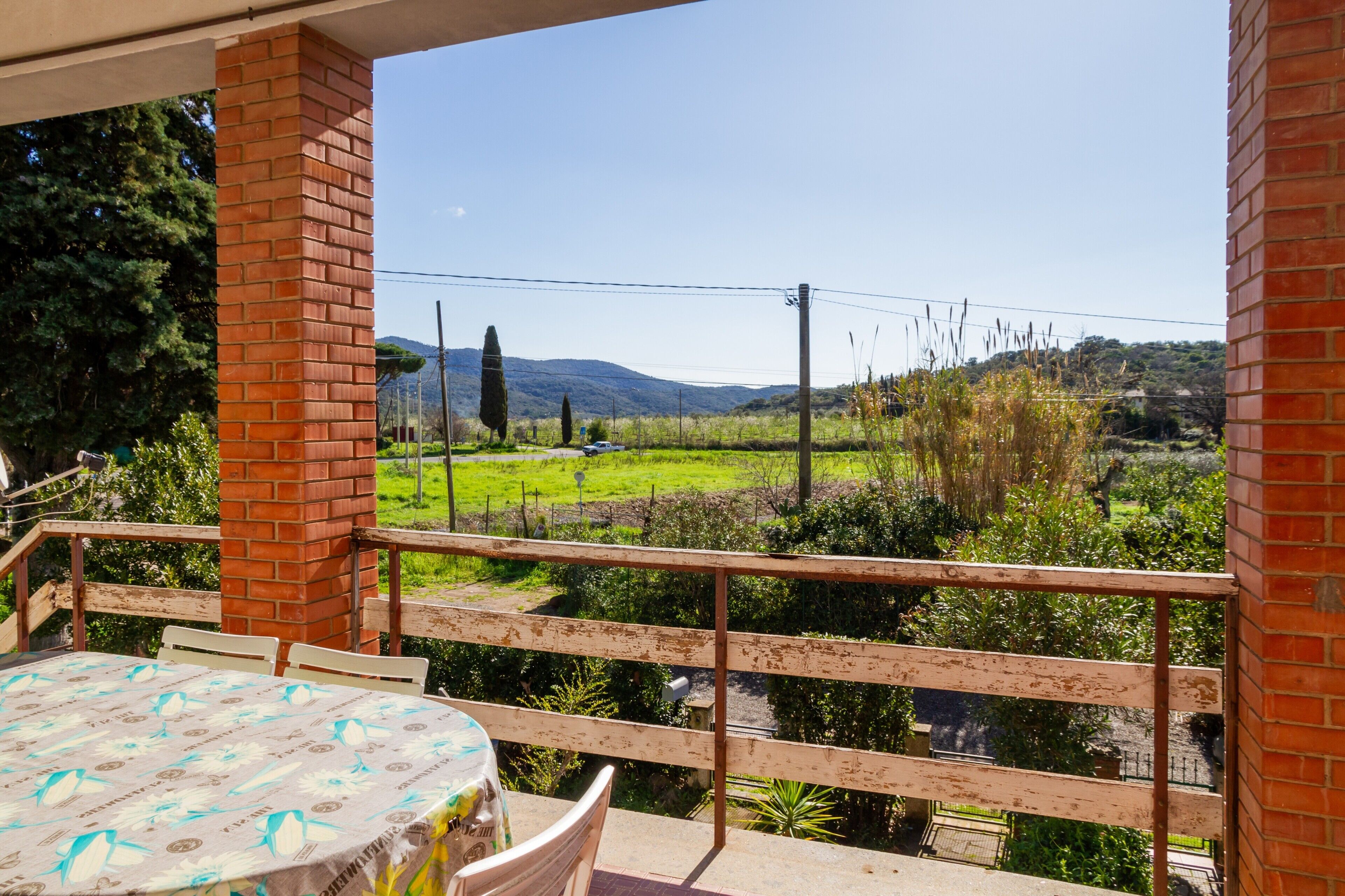 A balcony with a table and chairs, overlooking a green landscape with trees and a distant mountain.